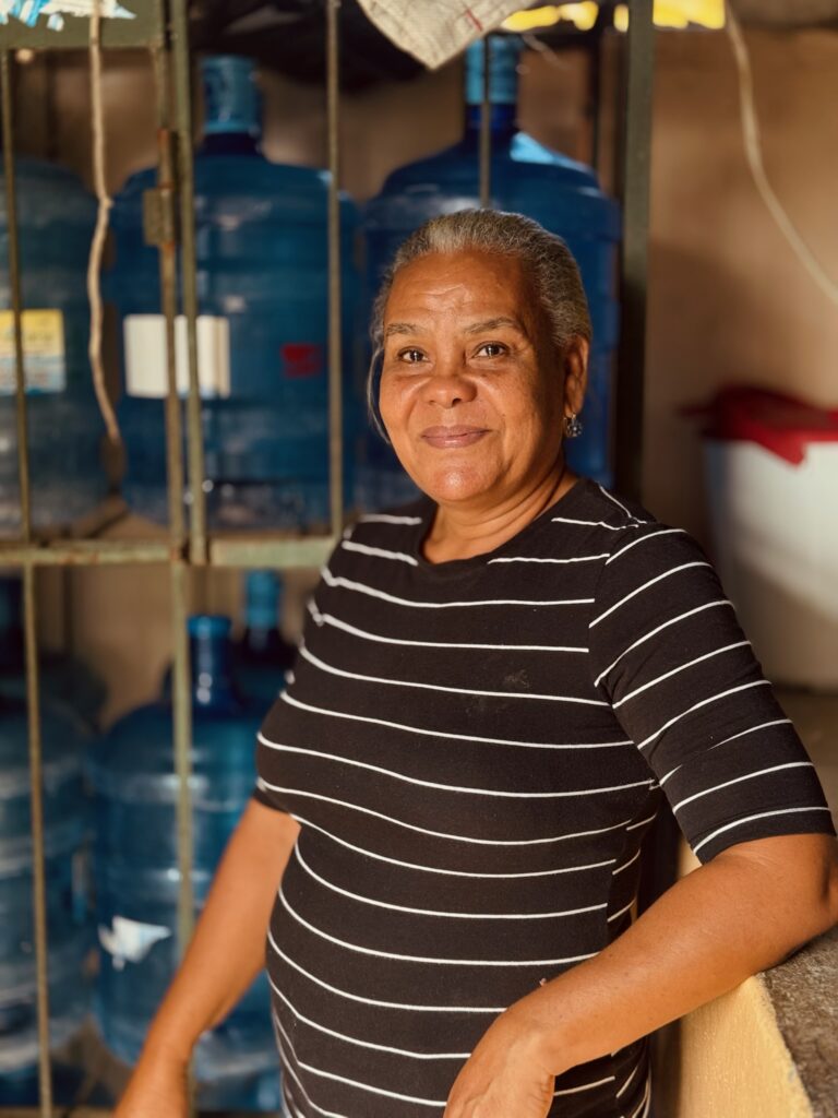 A woman smiles in front of gallons of clean water in the Dominican Republic